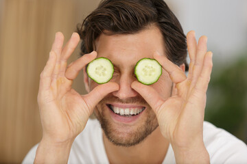 man putting sliced cucumber on his eyes