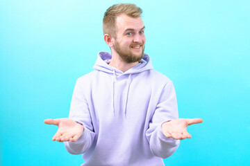 Man in a purple hoodie smiling and giving a imaginable gift in his hands on a blue background￼. Person. Hand. Palm. Holding. Gesture. Giving. Caucasian. Man. Open. Showing. Male. Empty