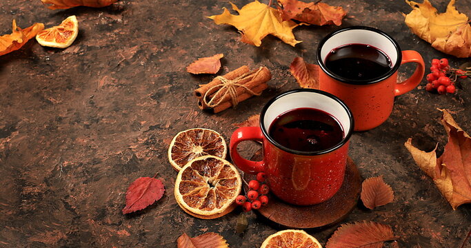 Two colored red and yellow enamel mugs with hot autumn drink, mulled wine and autumn fallen leaves on a rusty table, banner, hello autumn concept,