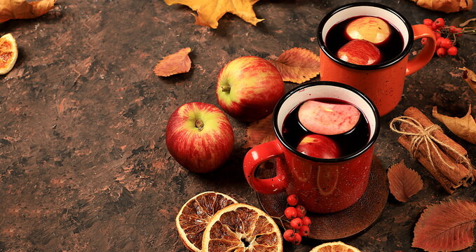 Autumn composition with colored enamel mugs with hot autumn drink, mulled wine with apples and fallen leaves on a rusty table, banner, hello autumn concept,