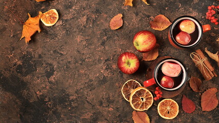 Two colored red and yellow enamel mugs with hot autumn drink, mulled wine and autumn fallen leaves...