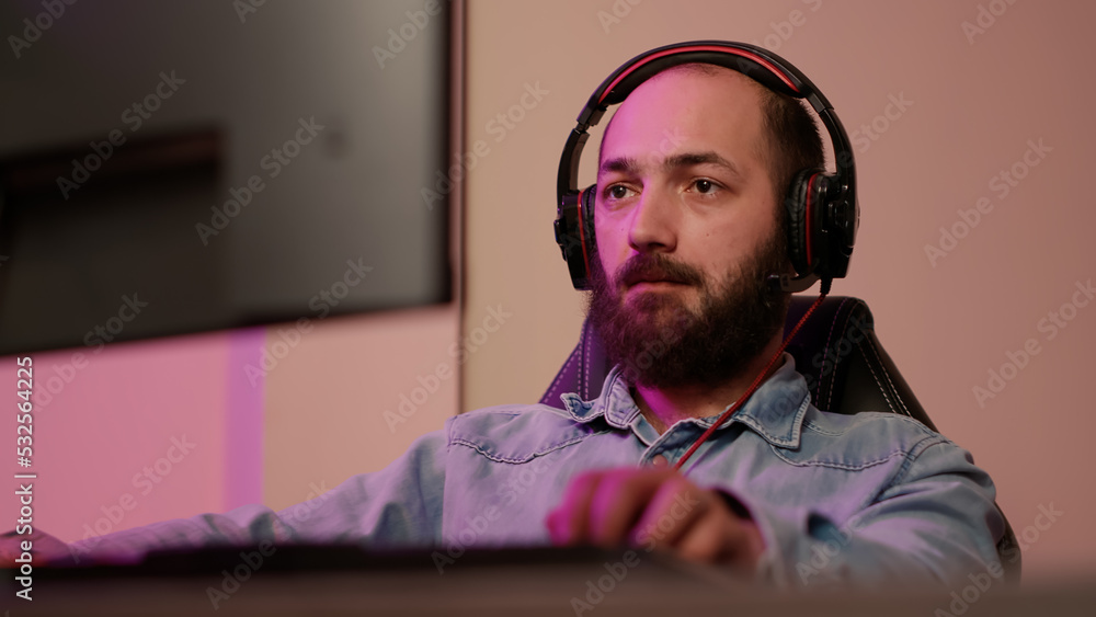 Poster handheld shot of man with gaming headset looking at computer screen and talking to team members whil