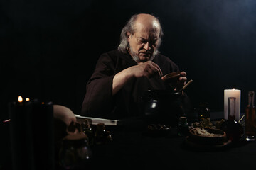 medieval alchemist preparing magic potion at night isolated on black.