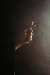 partial view of monk with holy cross in hand on black background with smoke.
