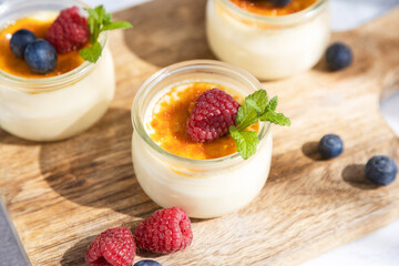 Close-up of a creme brulee dessert garnished with fresh sprig of mint and berries on a cutting board in bright sunshine.