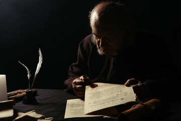 monk holding wax seal and manuscripts in darkness isolated on black.