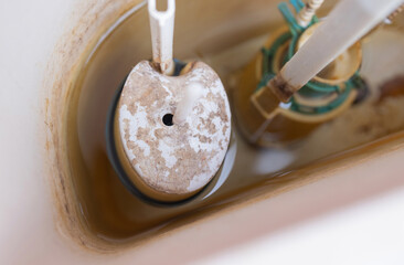 Toilet tank parts replacement. A man in orange gloves repairs the toilet tank drain.