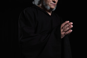 cropped view of bearded monk in cassock praying isolated on black.