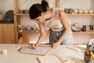 Female Entrepreneur Making A Weekly Plan In The Ceramics Shop