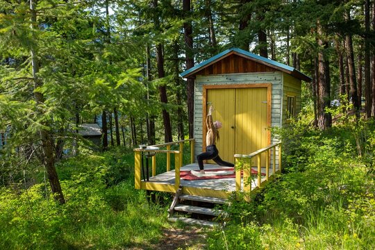 A woman is doing yoga on the balcony of her tiny cabin in the forest.