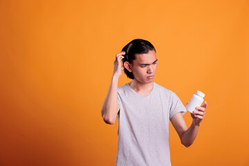 Asian young man confused about what pills to take, looking at tablets bottle. Disease treatment,...