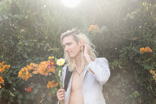 Stylish young man shirtless surrounded by flowers