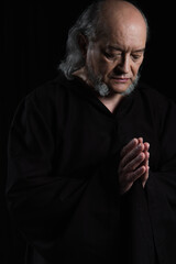 senior medieval monk in dark robe praying isolated on black.