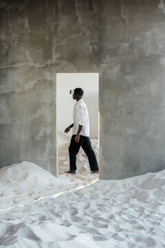 Young man in VR goggles walking in light room with sand