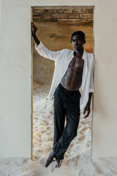 African young man in doorway in minimal studio with sand