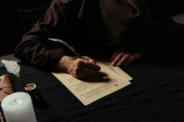 medieval monk with bowed head writing manuscript on parchment isolated on black.
