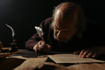 senior abbot writing manuscript on parchment isolated on black.