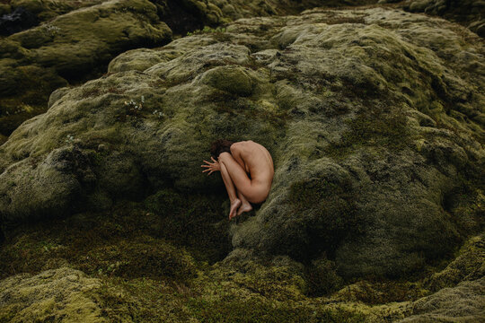 Young skinny woman in fetal position in the green moss in Iceland