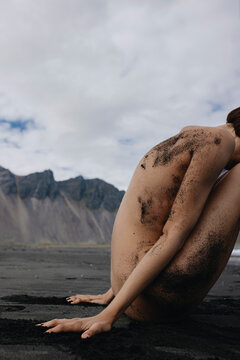 Naked girl sitting on sand near the sea in front of mountains Iceland