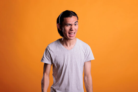 Angry young asian man with furious facial expression, showing negative emotions. Irritated person screaming, aggressive teenager looking at camera, front view studio medium shot