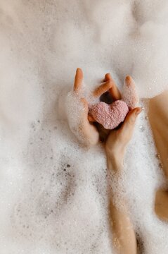 Unrecognizable female showing heart in foamy bath
