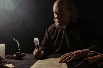 medieval priest in black robe writing manuscript on dark background.