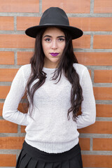 close up to the face of latin woman with long black hair, she wears a makeup and hat, in the background brick wall, beauty and fashion accessory