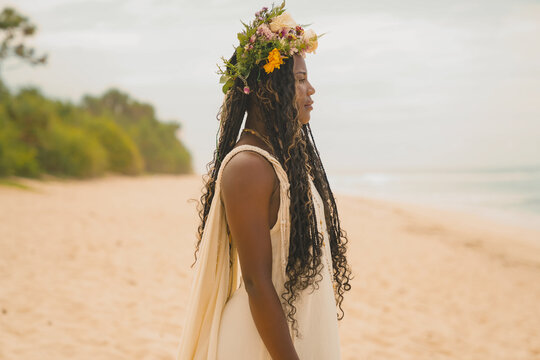 Black woman at the beach with a flower crown facing the ocean