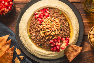 Arabic cuisine; Traditional creamy hummus dip with ground beef. Topped with olive oil, fresh pomegranate seeds, roasted pine nuts and parsley. Top view with close up.