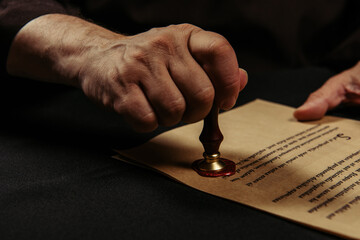 cropped view of monk stamping chronicle with wax seal isolated on black.