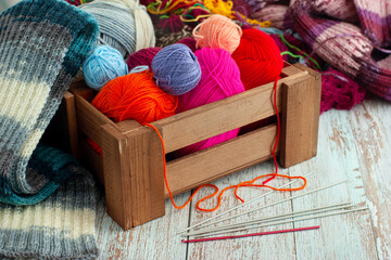 Balls of yarn in a wooden basket. Knitted scarf, colorful yarn and knitting needles on a wooden background. Knitting is a type of needlework.