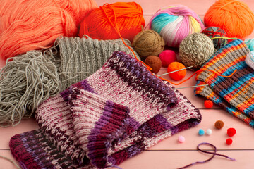 Balls of yarn in a wooden basket. Knitted scarf, colorful yarn and knitting needles on a wooden background. Knitting is a type of needlework.