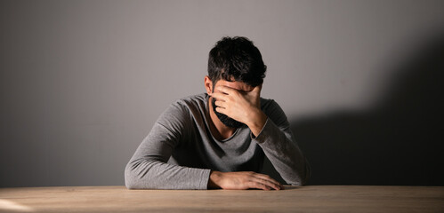 Obraz premium A man sits in front of a table covering his face with his hand