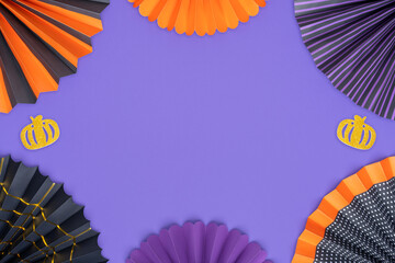 Halloween background from different paper fans and gold glitter pumpkins. A frame of Halloween decorations on a purple backdrop with copy space.