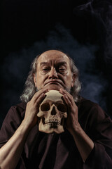 thoughtful religious philosopher looking at camera near human skull on black background.