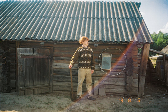 Curly-haired rustic red-haired guy stands with a shovel on the farm