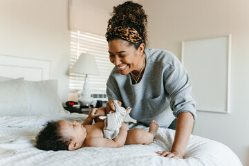 A mother with her baby son laying in the bed, changing his diaper