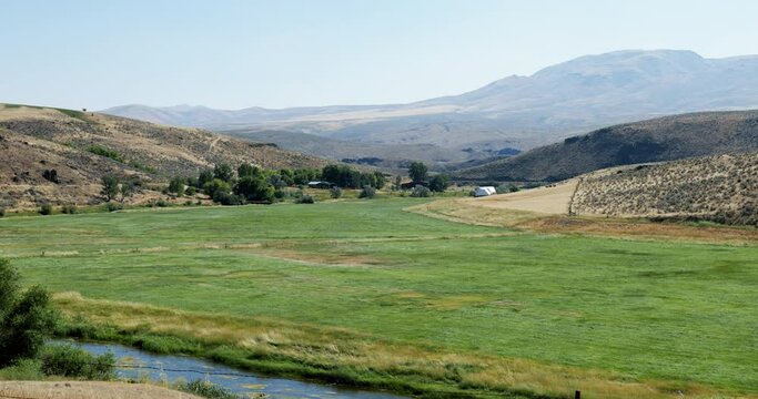 Homestead in the distance across a grassy meadow in the hills of eastern Oregon bordered by the Powder River