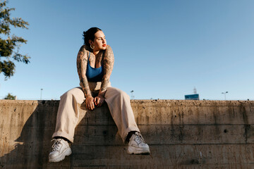 Tattooed woman sitting on stone border in summer