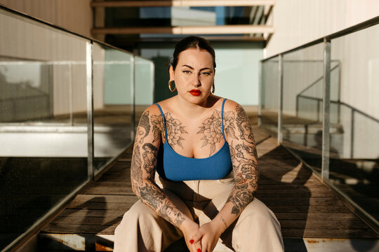 Tattooed plus size woman sitting on pathway in city