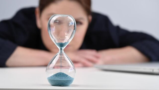 Business woman is bored, turns over the hourglass, opens the laptop and starts working.