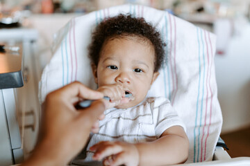 A close up of a father feeding his baby boy in a high chair