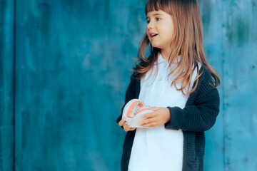 Toddler Girl Holding a Dental Orthodontic Teeth Model with Braces. Happy child learning about proper hygiene and treatment of teeth
