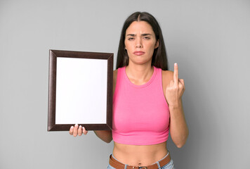 hispanic pretty woman feeling angry, annoyed, rebellious and aggressive with and empty frame