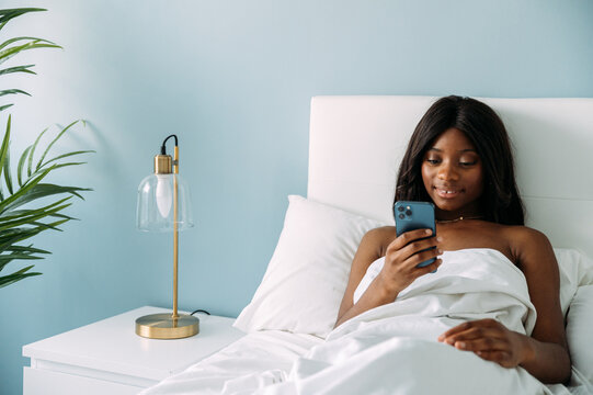 Black woman browsing smartphone on bed