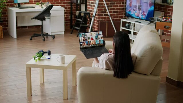 Freelancer working from home while discussing with coworkers on internet conference. Woman working remotely from home while in online meeting videocall on laptop sitting in living room.