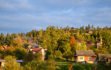 Fototapeta na wymiar Autumn Carpathian village landscape with guest houses on a mountain slope among colorful trees in the rays of the setting sun. Slavsko, Ukraine