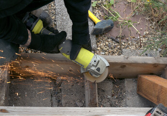 Sparks fly when a worker uses an angle grinder to cut away the top of a rusted nail, making the...