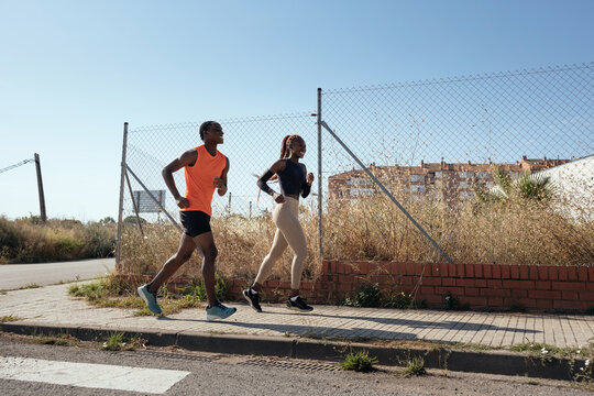 Black male and female athletes running near mesh fence