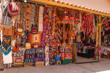 Souvenirs at the Pisac artisan market, Cusco, Peru.  Sale of souvenirs (ponchos, backpacks, clothes, blankets...).  Colorful ethnic market. - obrazy, fototapety, plakaty